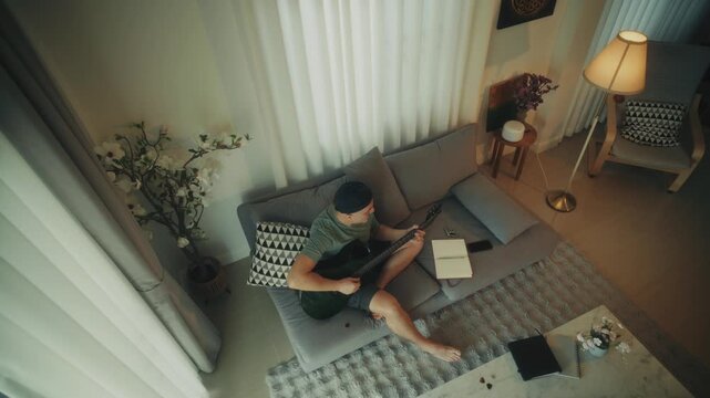 Man Creating Music. Person Sitting Barefoot Crafting Tunes With Acoustic Guitar And Notebook