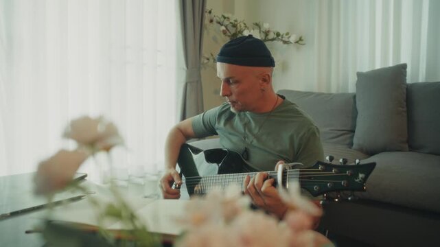 Calm Artist Strumming Guitar Near Flowers. Serene Man In Green Shirt Creating Melodies By Flowers