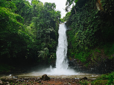 Tropical waterfall cascading into a rocky river surrounded by lush green forest in East Java, Indonesia