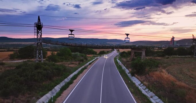 Aerial View of Fast Sports Car Driving Along Country Road Between Sunflower Field and Wheat at Sunset