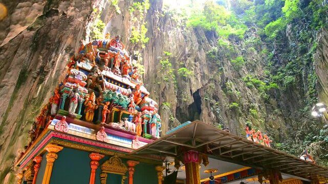 Hindu temple stands within the ancient limestone walls of Batu Caves in Malaysia. Natural light filters from the opening above, illuminating the colorful statues 