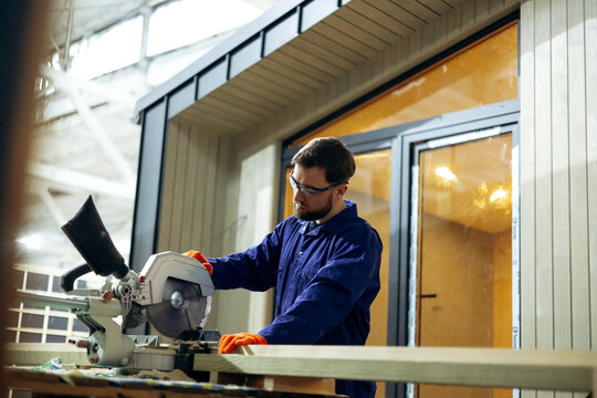 Male worker cutting wooden bars for modular buildings