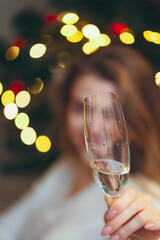 woman sits and drinks champagne against the background of a New Year tree