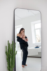young woman holding baby in her arms and looking in the mirror