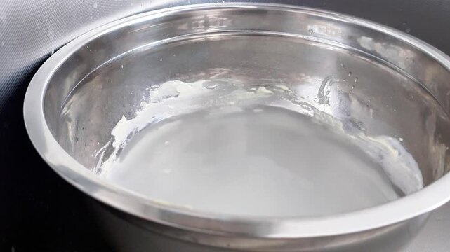 An iron bowl filled with dirty water rests in a sink, capturing a simple household moment that highlights everyday cleaning, washing, and kitchen utility in progress
