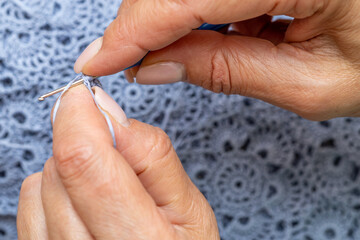 Close up of hands of unrecognizable woman knitting handmade clothes with spokes using  wool yarn....
