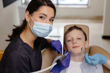 Kid in dental office. Dentist doing hygienic teeth cleaning to a boy sitting in a chair
