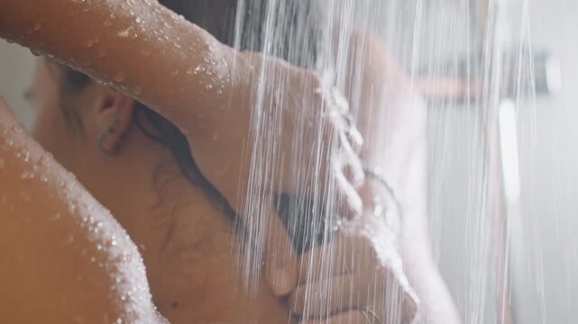 Hands massaging hair under hotel shower, fingers working shampoo through wet hair, droplets falling, soft light, boutique bathroom setting, guest enjoying selfcare, romantic getaway mood, spa