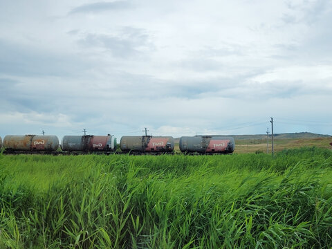 Novosibirsk, Russia - 02.03.2026, RGD, Freight train with tank cars on railway line, surrounded by green grass and cloudy sky. Industrial transport and logistics concept.