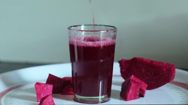 Close-up of fresh red beetroot juice being poured into a glass on a white tray