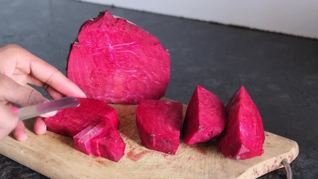 Close-up of hands slicing fresh red beetroot on a wooden cutting board