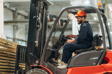 Driving, skilled employee. Warehouse worker operating a forklift while handling wooden materials © standret