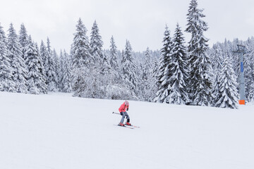 Lone young skier in a pink jacket descending a snowy slope at a winter mountain resort.