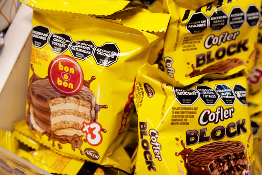 Yellow Arcor bon o bon and Cofler Block alfajore packages fill a retail shelf. Brands, product images, and nutritional warnings are prominent.