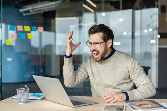 Angry man yelling at laptop experiencing work frustration