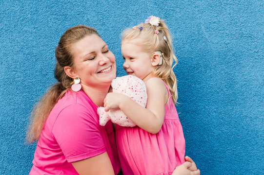 Deaf child with cochlear implant for hearing audio and aid for impairment having fun and laughs with mother outdoor in summer. Sound fitting device to help with communication listening and interaction