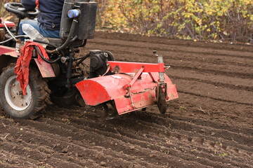 Man on red tractor, side view, rear part of tractor slightly from above, plow in soil during work, horizontal shot. © Anastasiia Harbar