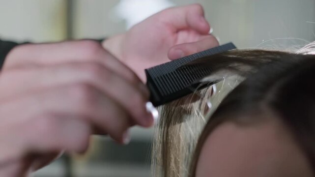 Close up of a hairdresser using a black comb to section brown hair for styling