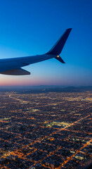 Fototapeta premium Aerial view of illuminated city lights at twilight, with aircraft wing visible. Represents exploration, travel and modern urban landscape concepts