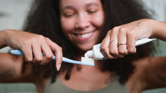 Happy Black Woman With Natural Hair Squeezing Toothpaste Onto a Toothbrush During Her Morning Routine
