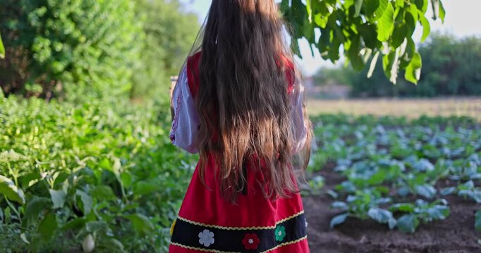 Bulgarian girl in ethnic folklore dress in a vegetable garden of bulgarian village, countryside of Bulgaria