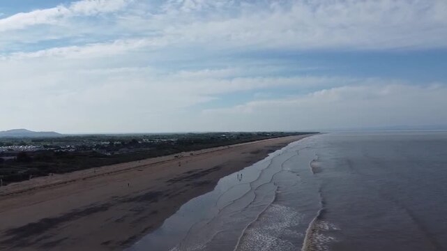 Forward flying drone tracking shot along Brean Sands beach heading towards the dramatic Brean Down headland on the UK coastline