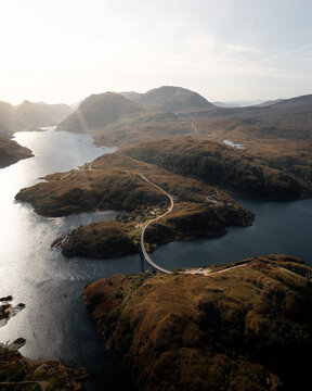 Aerial view of Kylesku Bridge curving gracefully over the dark waters and rugged landscape, Lairg, United Kingdom.