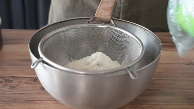 Chef sifting flour through sieve to aerate for sponge cake batter. Baking preparation and professional pastry technique in kitchen.