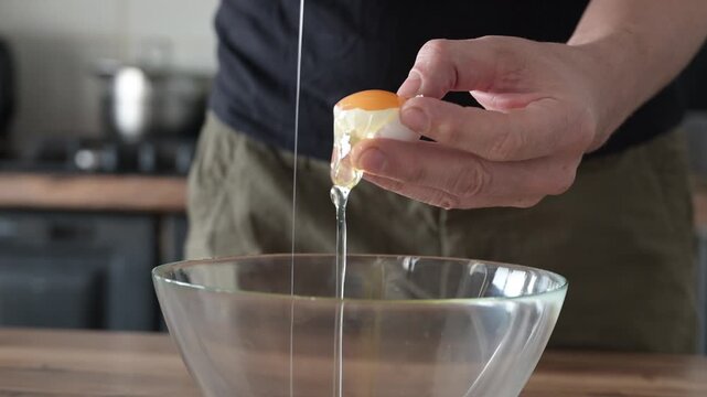 Mans hands cracking eggs into bowl to separate yolks from whites for sponge cake batter. Baking preparation and precise culinary technique.
