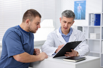 Fototapeta premium Urologist showing clipboard to patient at white desk in clinic