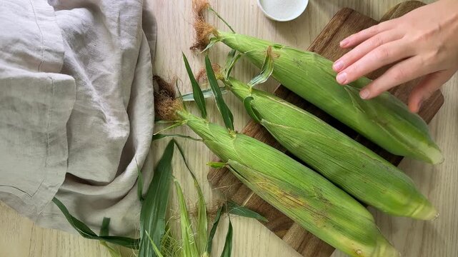 Fresh corn cobs on wooden board in rustic kitchen, overhead meal prep ingredients for summer barbecue and harvest season cooking, natural healthy food mood