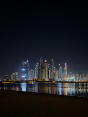 Fototapeta premium Vertical skyline of Dubai city skyscrapers at night, illuminated skyline with magical reflections on the Marina waterfront.