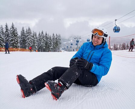 Male skier grimacing in pain while holding his injured knee on a snowy slope, winter sports accident, physical trauma, ski injury.