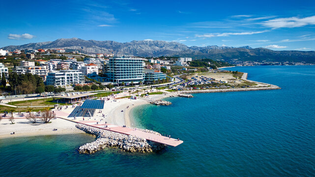 Aerial view of azure waters meet the sandy beach near Split's modern architecture, with the distant mountains providing a stunning backdrop, Split, Split-Dalmatia County, Croatia.