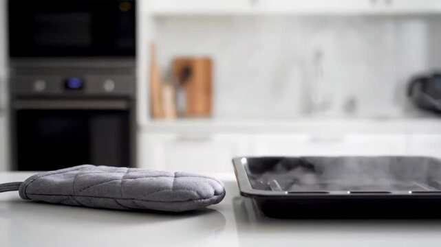 Hot baking sheet with steam and oven mitt on kitchen counter surface. Baking concept.