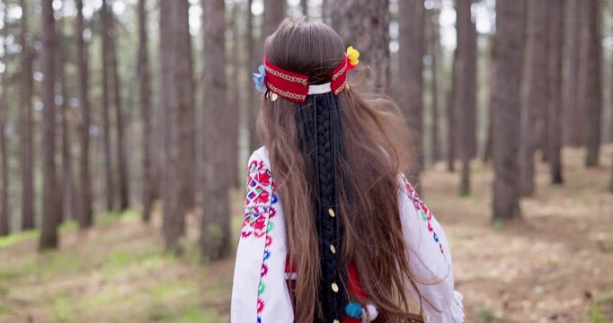 Beautiful bulgarian girl with ethnic folklore costume running behind trees on a trail in forest, Bulgarian beautiful nature