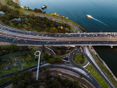 Aerial view of a bustling highway overpass cutting through Kings Park's verdant landscape, where the Swan River reflects the sky's azure hues, Kings Park, Western Australia, Australia.