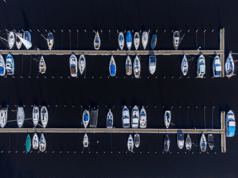 Aerial view of boats docked neatly in the marina, reflecting the clear sky, creating a striking contrast between the dark water and the bright hulls, Marina, Almere Haven, Flevoland, Netherlands.