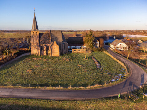 Aerial view of an ancient church standing proudly on a grassy hill, its spire piercing the clear sky, Persingen, Gelderland, Netherlands.