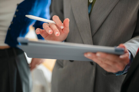 A person in a suit holds a stylus and tablet, engaging with digital information during a business meeting.