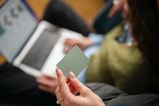 A person holds a payment card while using a laptop, suggesting online shopping or financial management.