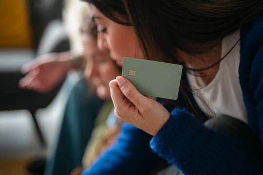 A woman holds a green payment card, with another person blurred in the background. The card has a chip and a network logo.