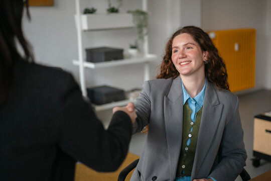 Two professionals shake hands in an office setting, signifying a successful meeting or agreement.