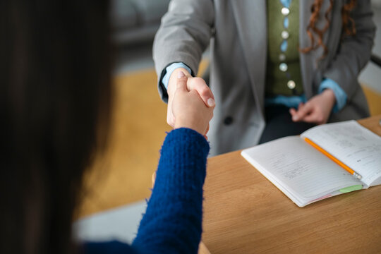 Two people shake hands over a desk with an open notebook and pencil, signifying agreement and partnership.