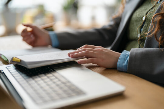 A person in professional attire reviews documents at a desk with a laptop, focusing on their work.
