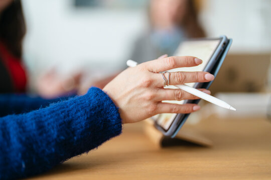 A person's hand, adorned with rings, holds a stylus to a tablet screen, suggesting digital work or creativity.
