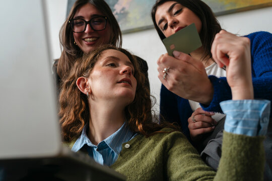 Three women collaborate on a purchase, one holding a payment card while others look on with interest.