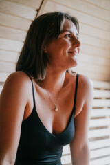 A woman is sitting in a room with a smile on her face. She is wearing a black tank top and a necklace