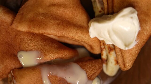 This appetizing close-up shot captures a rustic serving of golden-brown thin pancakes, likely blini or crepes, folded into triangular shapes. 