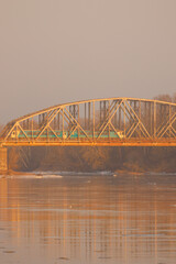 Train travels on an old railway bridge over a river at sunset